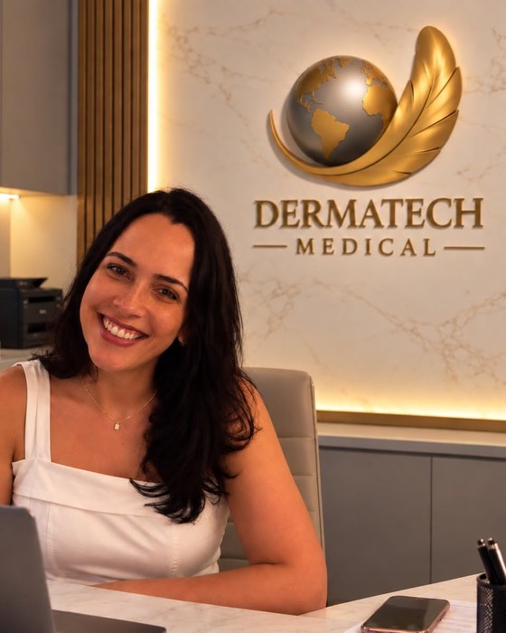Luciana, fundadora da Dermatech Medical, sentada à sua mesa no escritório da empresa, com o logotipo da marca na parede atrás.